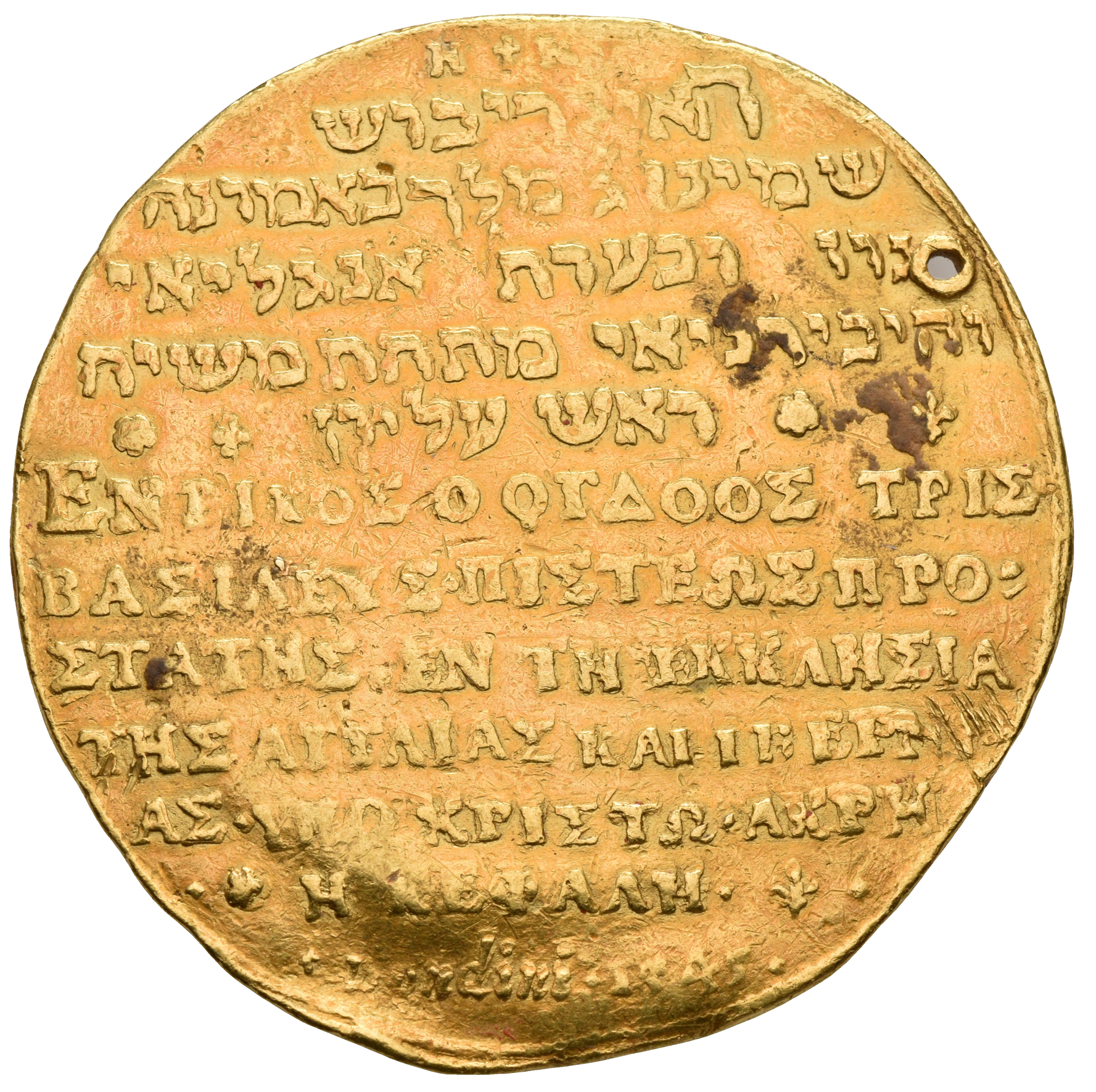 Close-up of a round gold coin with Hebrew inscriptions and a small hole on the right side; worn, textured surface.